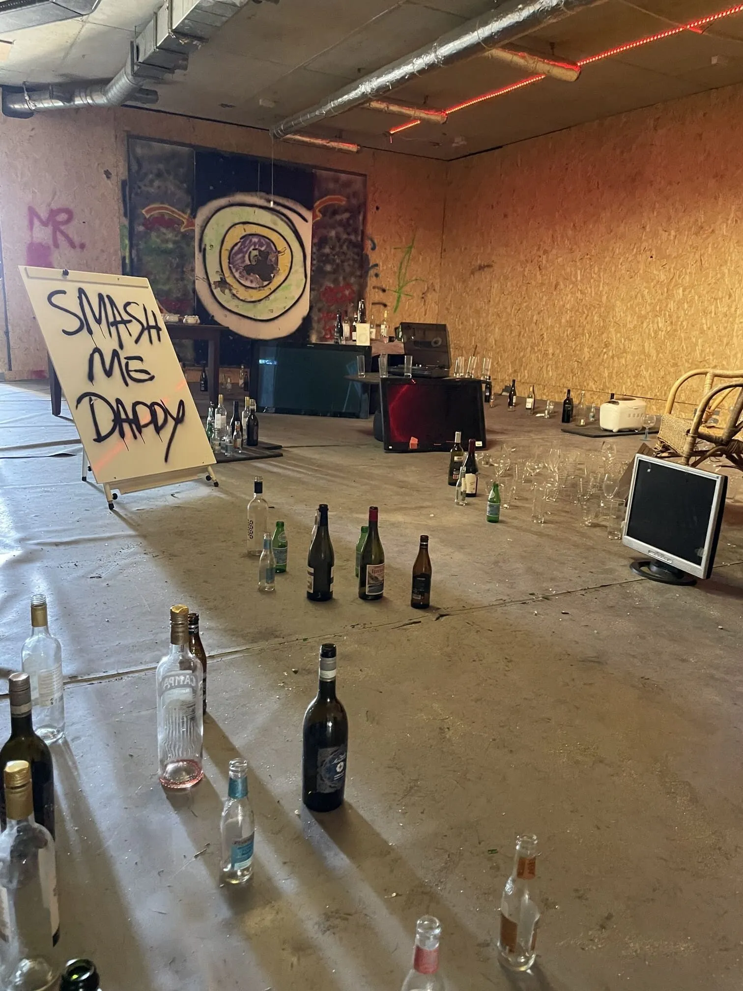 Rage room setup with bottles, target art, and “Smash Me Daddy” sign